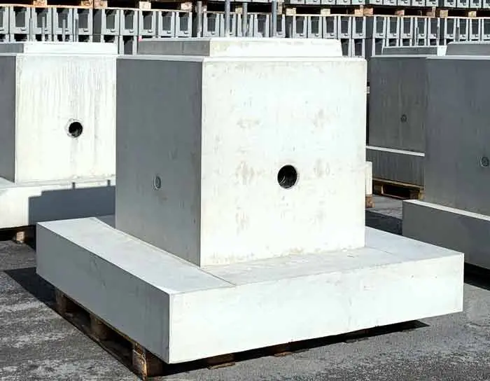 Ein Betonfundament mit quadratischer Form und einer zentralen Aussparung für Rohre oder Anschlüsse.