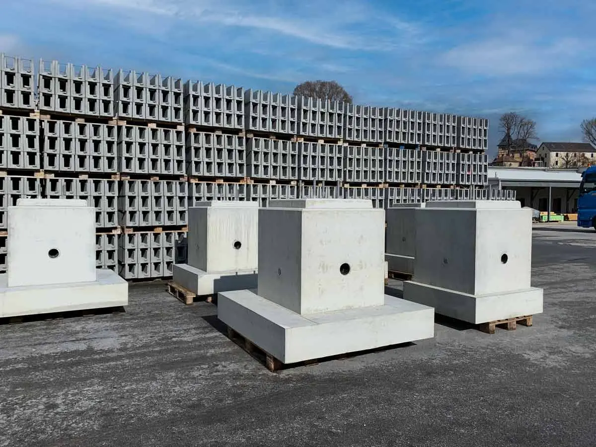 Betonfundamente auf Holzpaletten in einem Lagerbereich mit weiteren Betonobjekten im Hintergrund.