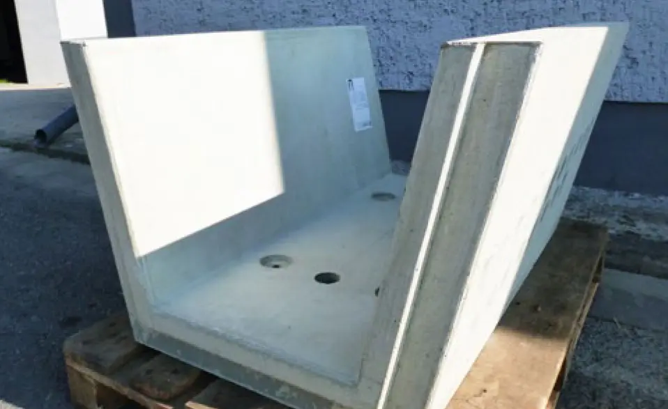Betonschale mit zwei Öffnungen auf einer Holzpalette, in neutraler Umgebung.