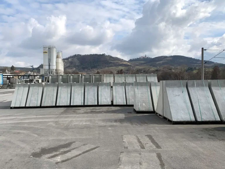 Reihe von Betonfertigteilen, die auf einem Lagerplatz aufgestellt sind, mit Hügeln im Hintergrund.