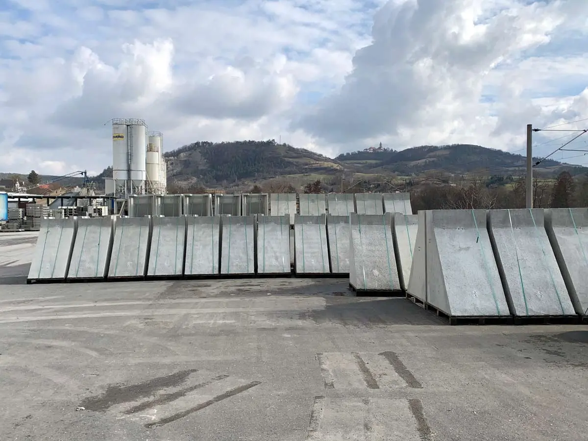 Reihe von Betonfertigteilen, die auf einem Lagerplatz aufgestellt sind, mit Hügeln im Hintergrund.