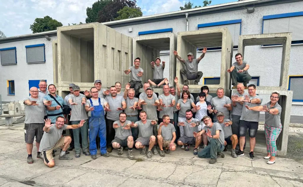 Gruppenfoto von Mitarbeitern in Arbeitskleidung, die vor großen Betonformen stehen.