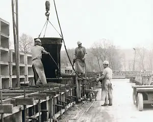 Drei Arbeiter, die an einer Betonproduktionsstätte mit einem Kran und Formen arbeiten.