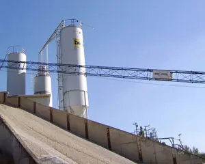 Zementlager mit mehreren weißen Silos und einer blauen Förderbrücke im Vordergrund.
