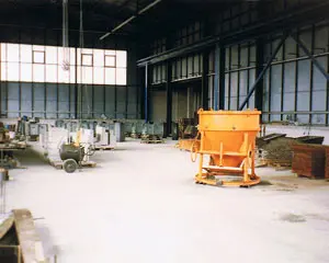 Blick auf eine Bauwerkstatt mit einem orangefarbenen Mischer und verschiedenen Maschinen im Hintergrund.