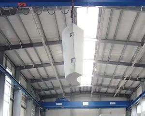 Ein hängendes Bauteil wird in einer Industriehalle von einem Kran gehalten.