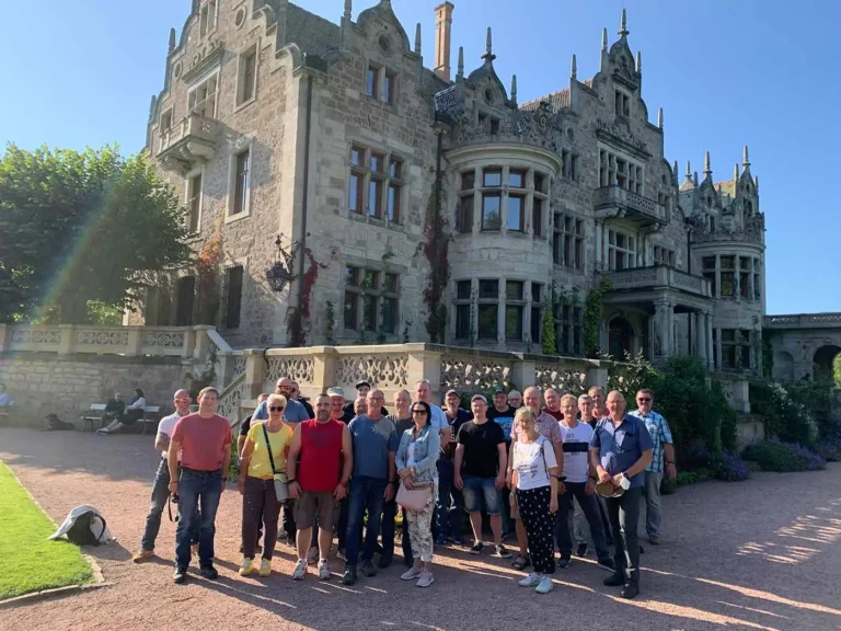 Eine Gruppe von Menschen steht vor einem historischen Schloss mit einer detaillierten Architektur und einem klaren Himmel.