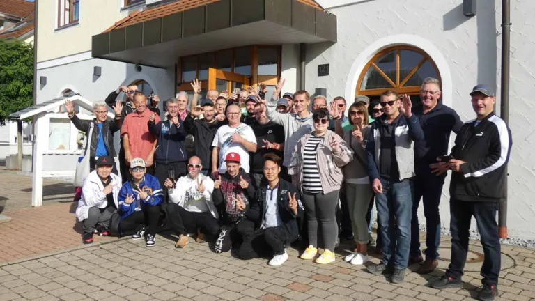 Eine Gruppe von Personen posiert vor einem Gebäude, einige zeigen Peace-Zeichen.