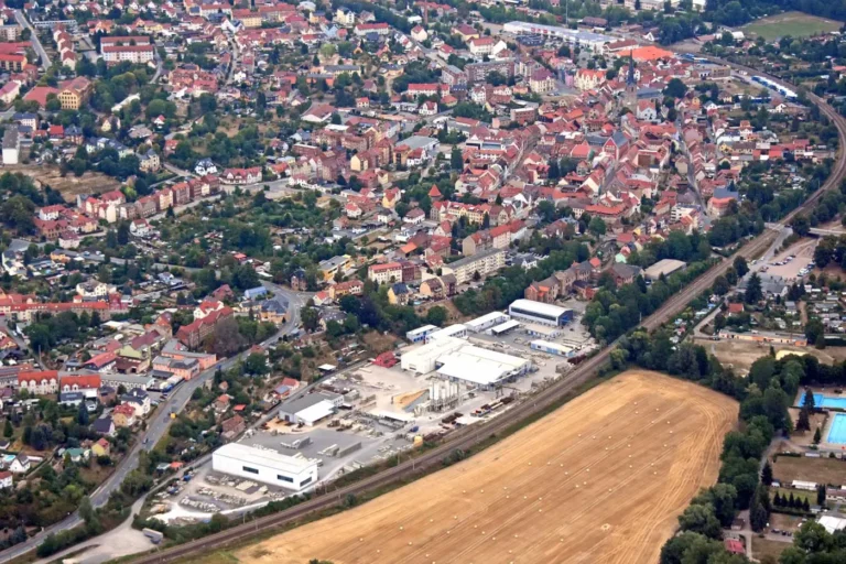 Luftaufnahme einer Stadt mit roten Dächern, Wohngebieten und einem Industriegebiet im Vordergrund.