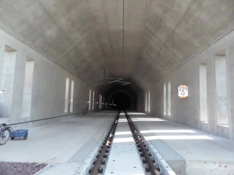 Tunnel mit Schienen, der in die Dunkelheit führt, mit Betonwänden und einer Nummernschilderkennung.