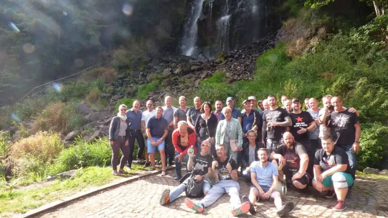 Eine Gruppe von Menschen posiert vor einem Wasserfall in einer natürlichen Umgebung.