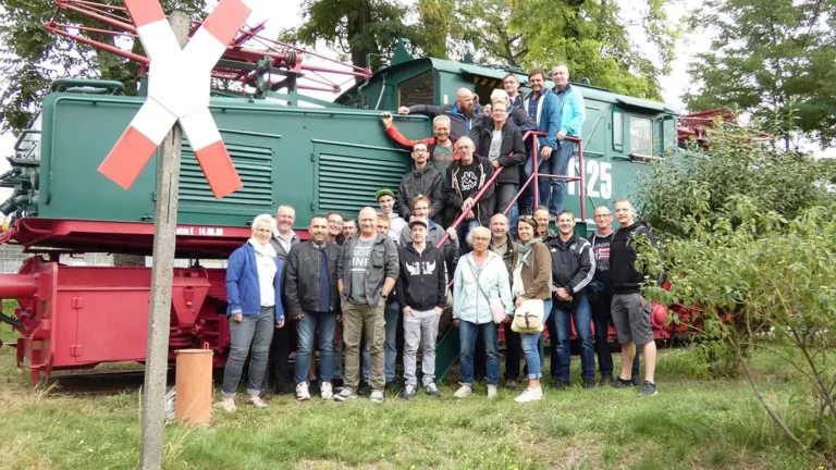 Eine Gruppe von Menschen posiert vor einer historischen Lokomotive mit der Nummer 25.