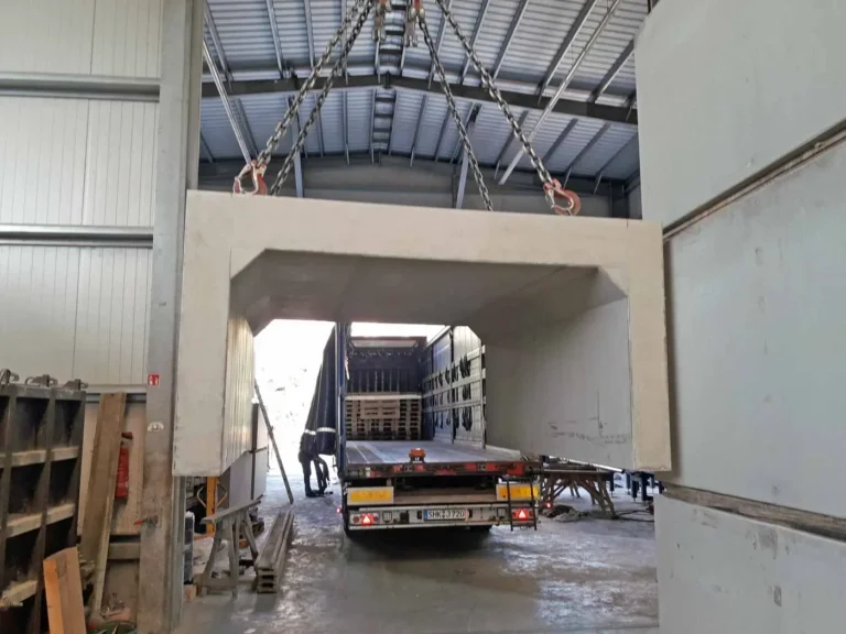 Ein Betonfertigteil wird mit einem Kran über einen Lkw gehoben in einer Industriehalle.