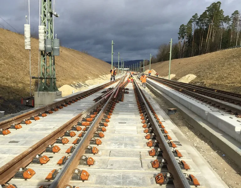 Gleisbauarbeiten auf einer neuen Bahnstrecke mit mehreren Schienen und Bauarbeitern.